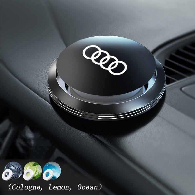 Round black Audi rings air freshener on a car dashboard, with Cologne, Lemon and Ocean refill options shown below.